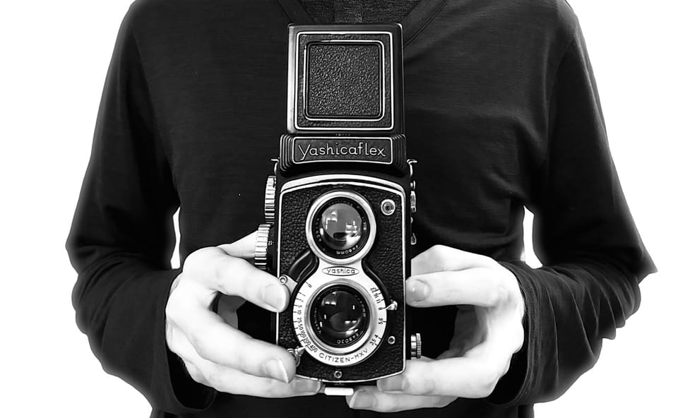 The author holds a 1954 Yashicaflex A2 film camera at chest level, with the viewfinder up.